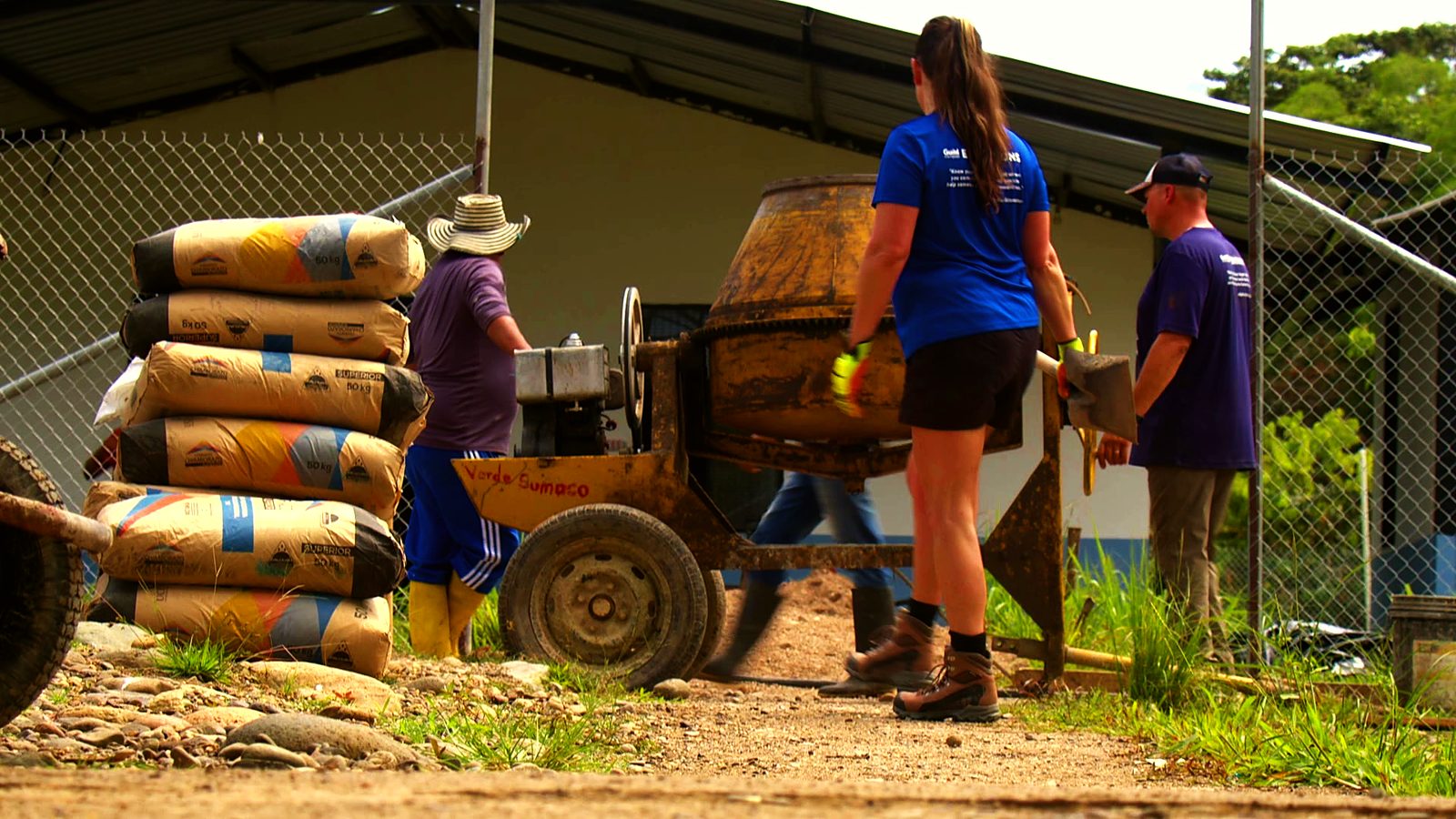 volunteers working the cement mixer beside a stack of cement bags